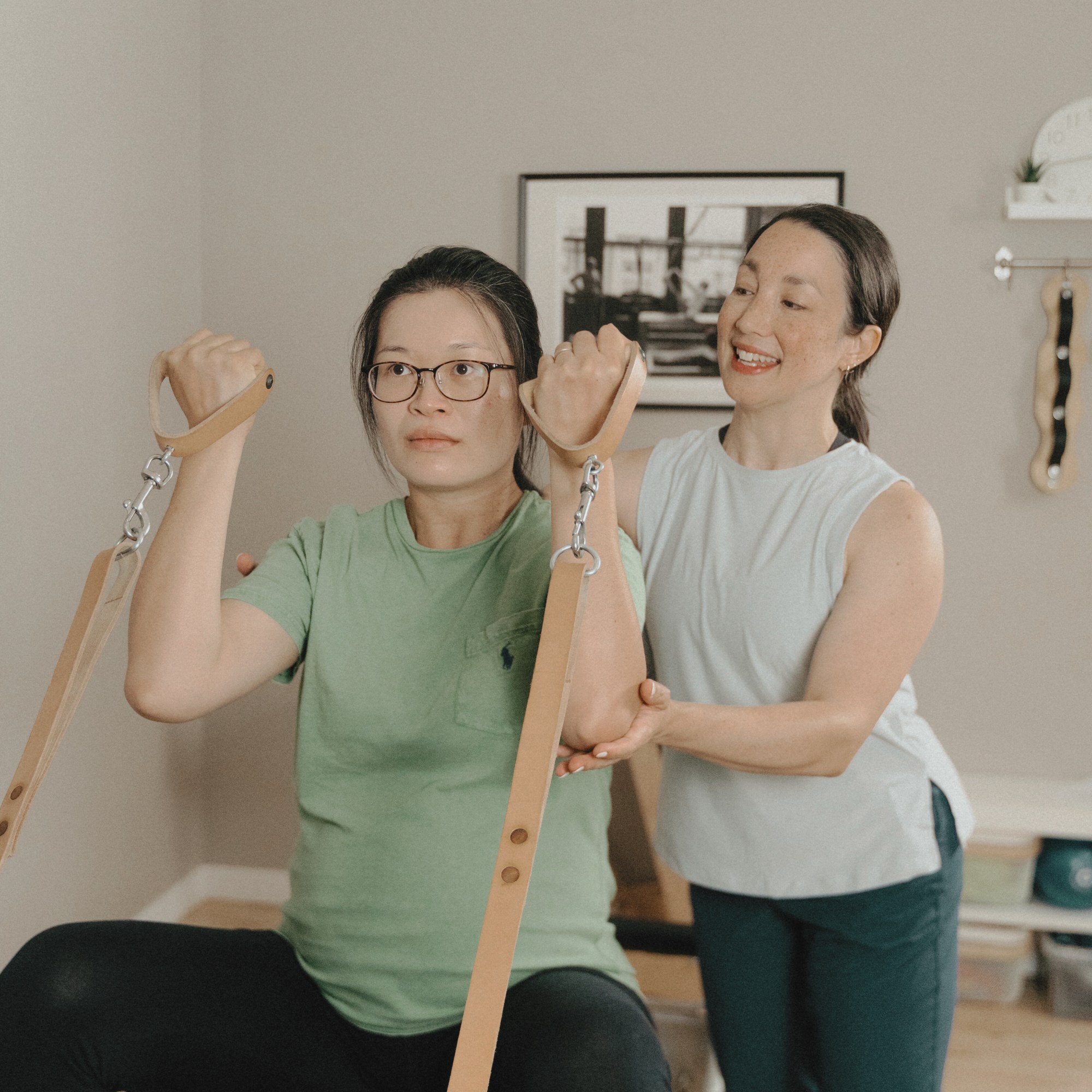 Instructeur de Pilates guidant une cliente enceinte dans un exercice de renforcement du haut du corps sur le Reformer.