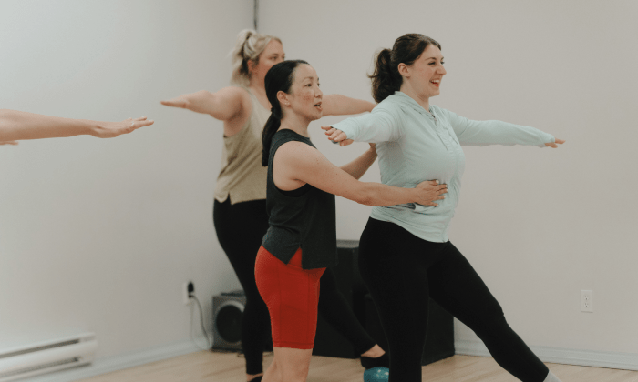 Instructeur de barre fitness dirigeant un cours en groupe dans une flexion latérale debout avec des poids légers/haltères dans le cadre d'un entraînement de barre à St-Henri, Montréal.