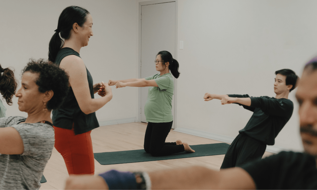 Instructeur de barre fitness à St-Henri, Montréal, enseignant un exercice sur tapis en position agenouillée à un groupe lors d'un cours de barre.