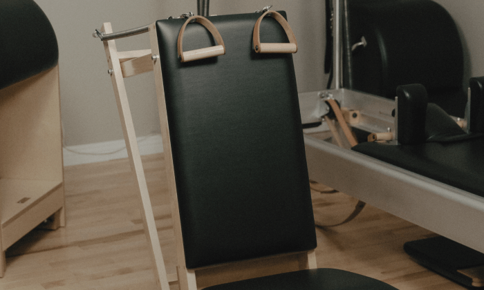 Gros plan sur la petite chaise Pilates (Baby Chair) dans un studio privé à Montréal, mettant en valeur son siège incliné, sa structure en bois, ainsi que ses poignées en bois et cuir fixées à des ressorts.