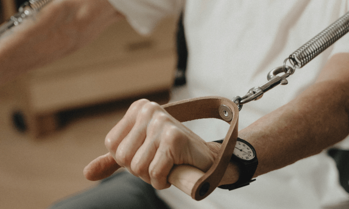 Gros plan sur la main d’une cliente tenant la poignée en bois et cuir d’un Small Arm Chair (Baby Chair) de Pilates, exécutant l’exercice Boxing et étirant le ressort lors d’une séance privée de Pilates classique à Montréal.