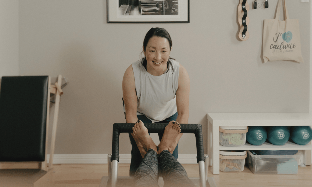 Instructrice guidant les pieds d’une cliente sur le footbar du Reformer lors d’une séance privée de Pilates classique à Montréal, pendant l’exercice Footwork Tendon Stretch.