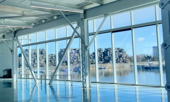 Vue intérieure du pavillon du Grand Quai dans le Vieux-Montréal avec de grandes fenêtres donnant sur le fleuve Saint-Laurent et Habitat 67, futur lieu de l’événement Les 100 ans du Pilates Montréal.